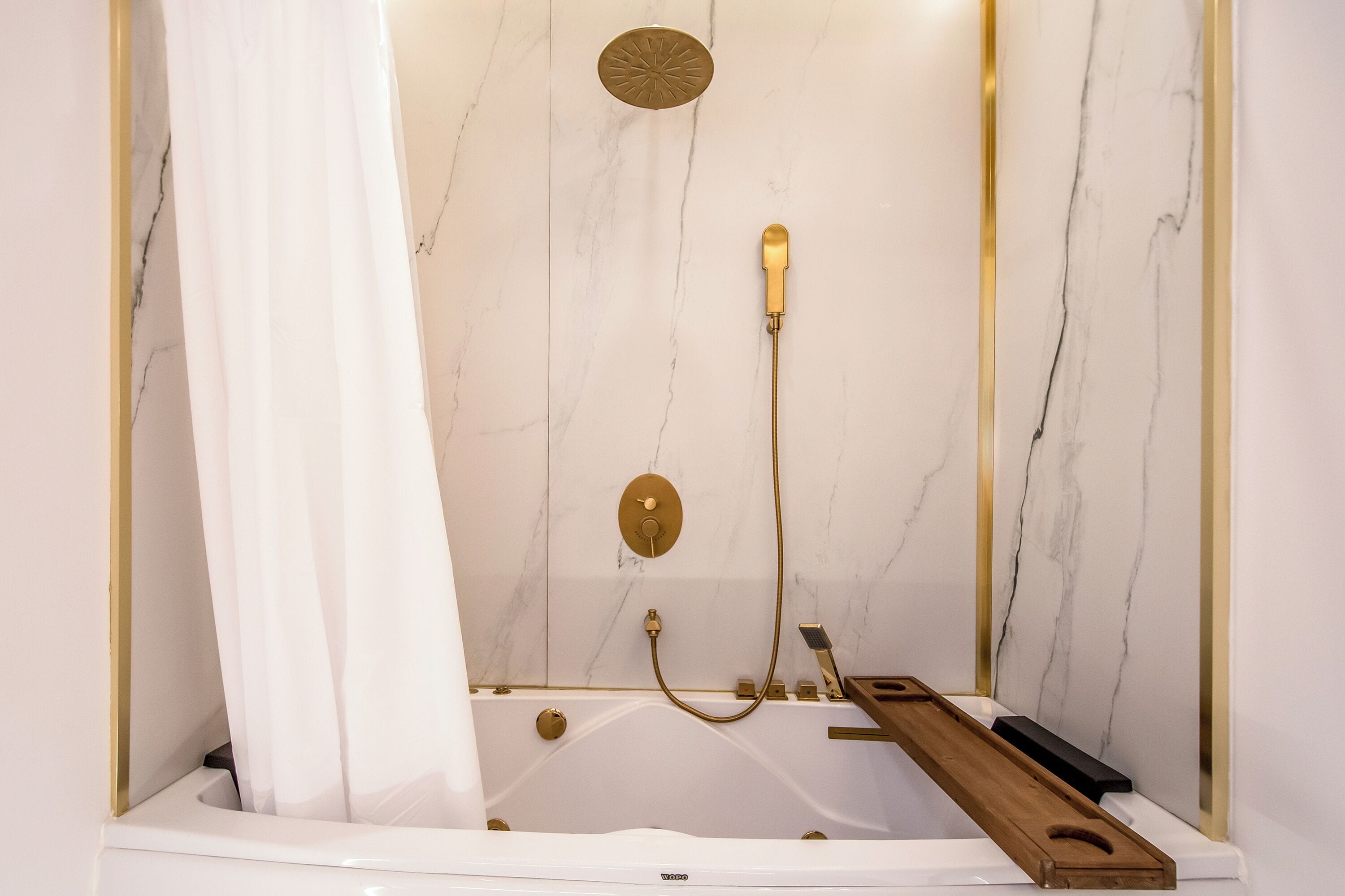 A bathroom with a white bathtub, gold fixtures, and a marble wall.