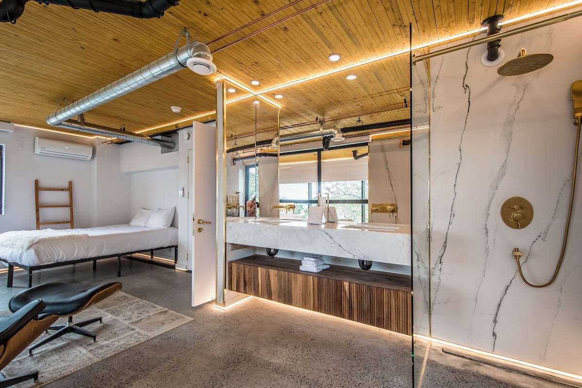 Habitación de hotel moderna con techo de madera, un espejo grande, pared de mármol, ducha y cama.