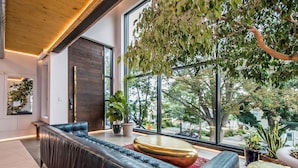 A modern living room with a leather sofa, a round coffee table, and a large window with a view of trees and buildings.