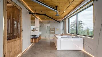 A modern bathroom with a large window, a bathtub, and a wooden door.