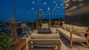 A rooftop terrace with a sofa, chairs, and a coffee table, decorated with string lights.