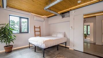 A modern bedroom with a wooden ceiling, a bed, a potted plant, and a large window.