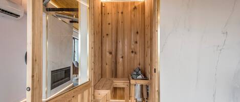 A wooden sauna with a bench and a table, a mirror, and a small shelf with items.