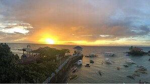 A coastal scene with a sunset, boats, and a pier with a gazebo. - CNC DIVE RESORT (Lapu-Lapu)