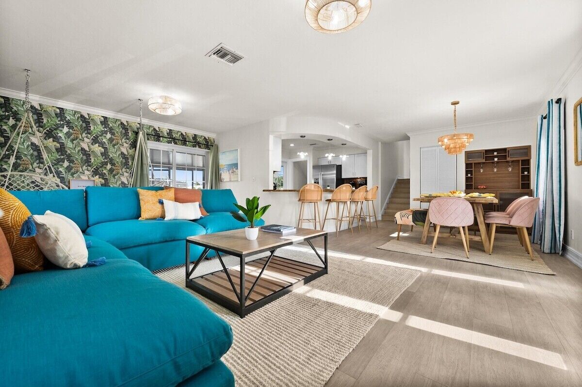 Ein modernes Wohnzimmer mit einem türkisblauen Sofa, einem Couchtisch und einem Essbereich mit Tisch und Stühlen.