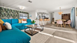 A modern living room with a teal sofa, a coffee table, and a dining area with a table and chairs.