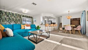 Ein modernes Wohnzimmer mit einem türkisblauen Sofa, einem Couchtisch und einem Essbereich mit Tisch und Stühlen.