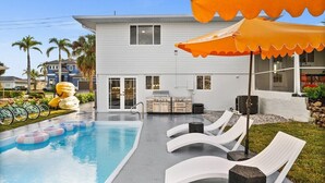 Una piscina con lettini e zona barbecue, circondata da un edificio residenziale.