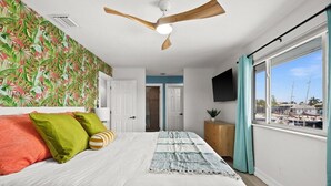 A bedroom with a bed, a ceiling fan, a window with curtains, and a wall-mounted TV.