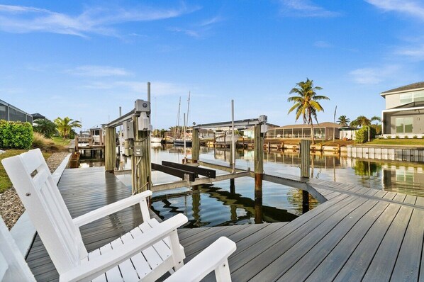 A waterfront property with a wooden dock, white chairs, and a modern building.