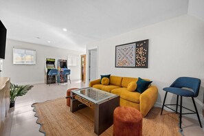 A modern living room with a sofa, coffee table, and a foosball table. There is a bar area with chairs and a TV. - Waterfront 4BR, Heated Pool, Hot Tub and Sauna (Marco Island)