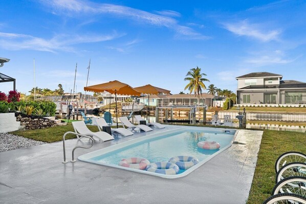 A swimming pool with lounge chairs, umbrellas, and a clear sky.