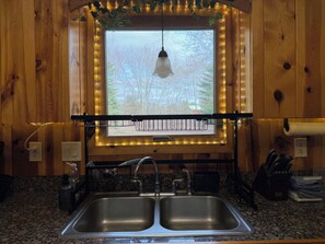 A kitchen with wooden walls, a double sink, and a window with a view of trees. - Relax near CMU and Casino with hot tub and fireplace (Mount Pleasant)