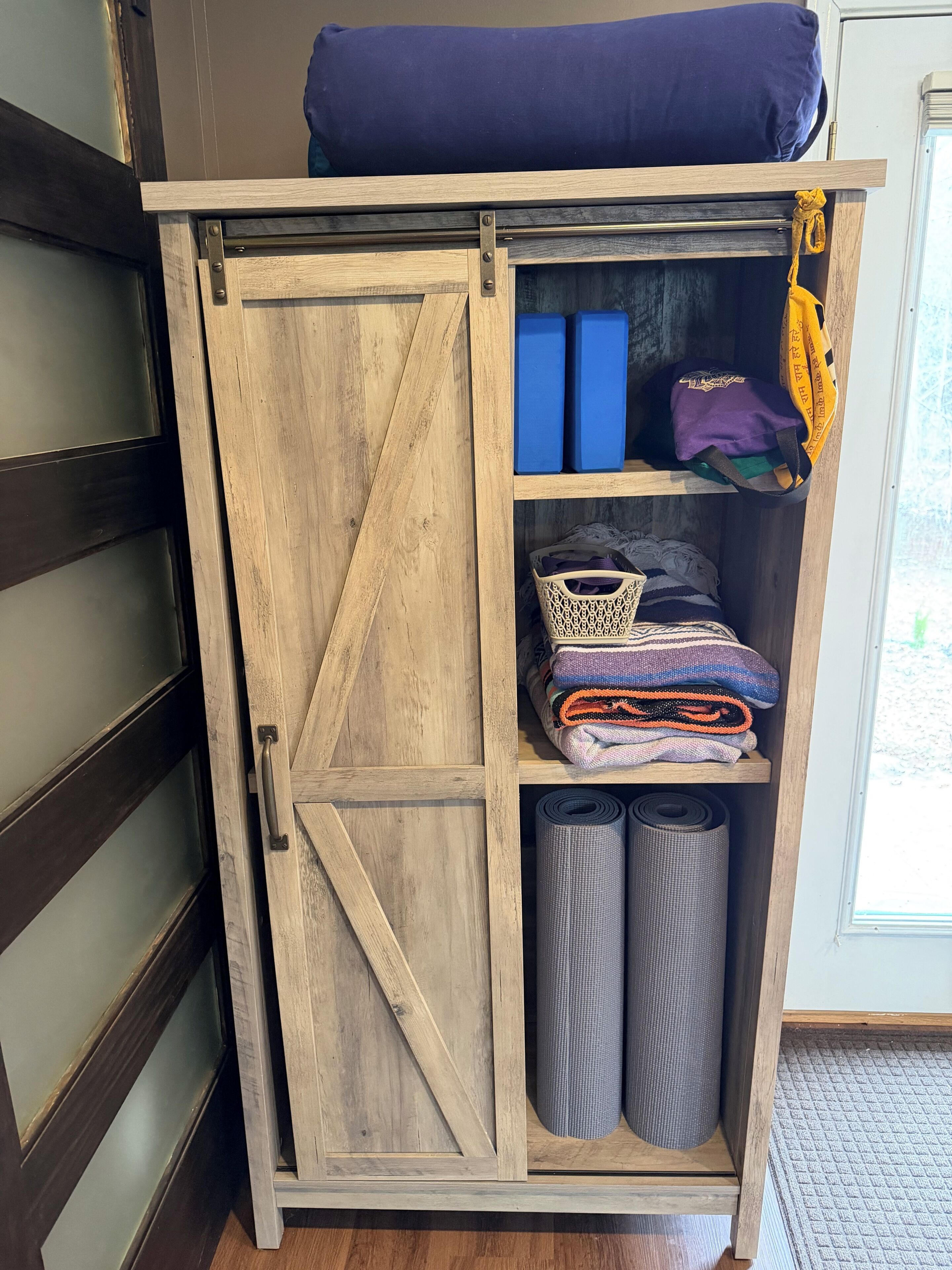 A wooden cabinet with a sliding door, containing folded blankets, rolled rugs, and storage boxes.