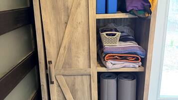 A wooden cabinet with a sliding door, containing folded blankets, rolled rugs, and storage boxes.