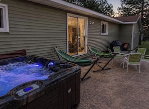 A hot tub, a hammock, and patio chairs outside a house.
