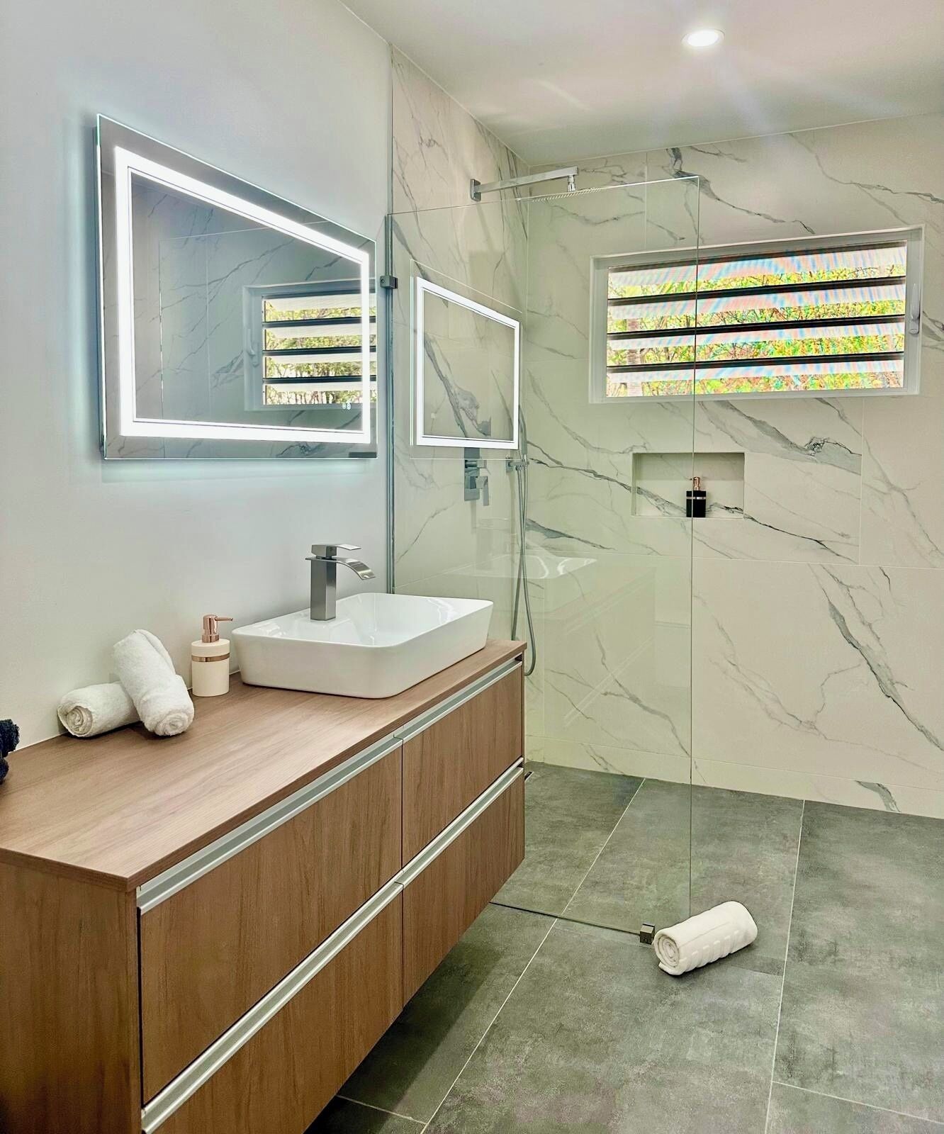 A modern bathroom with a marble vanity, a glass shower enclosure, and built-in lighting.