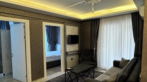Een moderne woonkamer met een bank, salontafel en een aan de muur bevestigde televisie. Er is een schuifdeur die leidt naar een andere kamer.