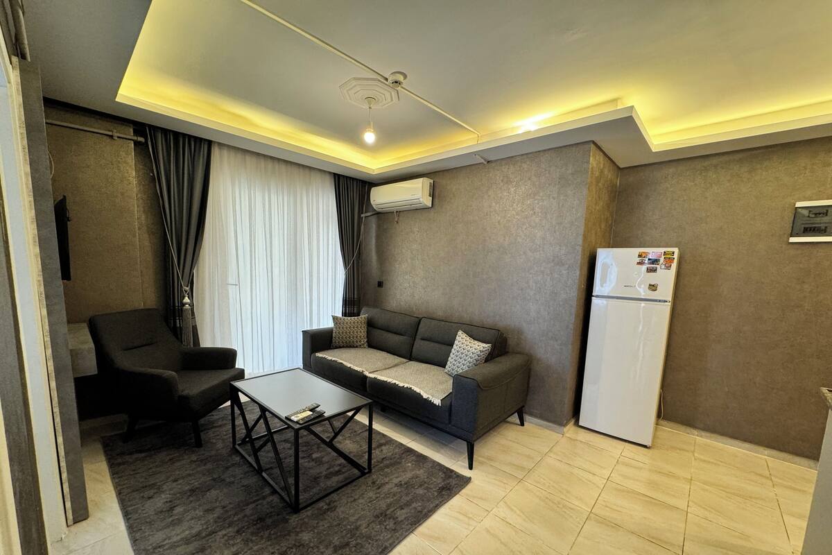 A modern living room with a sofa, armchair, coffee table, and a refrigerator.