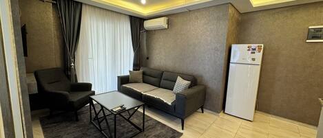 A modern living room with a sofa, armchair, coffee table, and a refrigerator.
