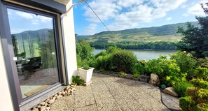 A modern building with a glass door, a gravel patio, and a view of a lake and hills.