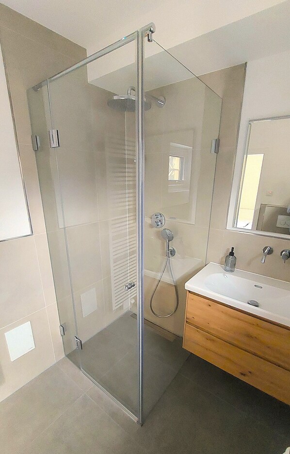 A modern bathroom with a glass-enclosed shower, a wooden vanity, and a large mirror.