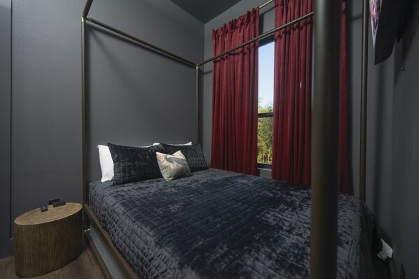 A bedroom with a four-poster bed, dark walls, and red curtains.