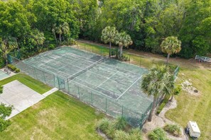 Un court de tennis entouré d’arbres et délimité par une clôture blanche.
