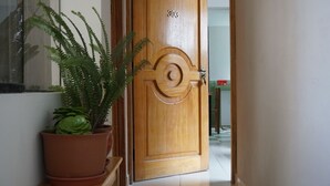 A wooden door with the number 303, a potted plant, and a checkered floor.