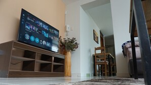 A living room with a flat-screen TV on a wooden stand, a vase with flowers, and a wooden chair.