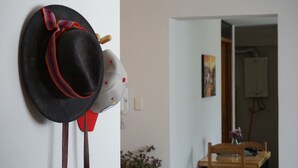 A room with a wall-mounted hat rack holding two hats, a wooden chair, and a table with a vase of flowers.