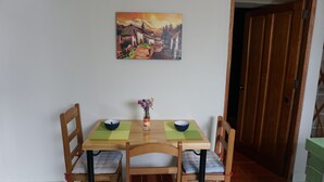 A dining area with a wooden table and chairs, a painting on the wall, and a door in the background.