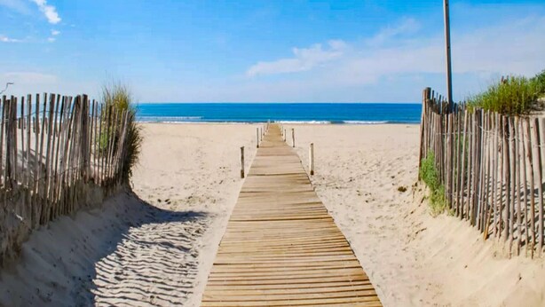 Ein Holzsteg führt zu einem Strand unter blauem Himmel.
