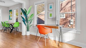 Een moderne eethoek met een houten tafel, groene en oranje stoelen en een grote potplant.