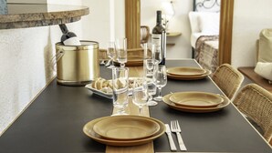 A dining table set with plates, glasses, and cutlery, with a gold-colored container and a bottle in the background. - Apartment Sunset Moraira City (Moraira)