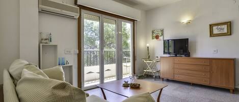 Ein Wohnzimmer mit einer Couch, einem Fernseher, einem Schrank und einer Glastür zum Balkon.