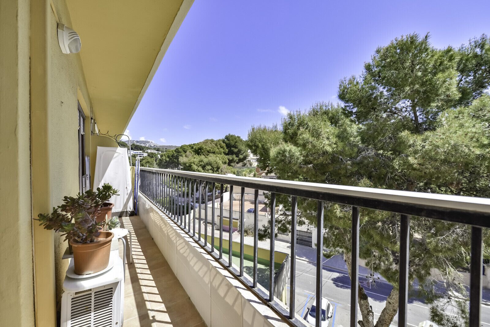 A balcony with a view of a parking area and trees.