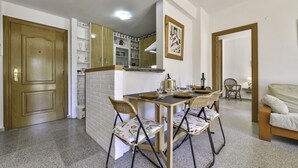A compact kitchen with a dining area, wooden cabinets, and a small table with chairs. - Apartment Sunset Moraira City (Moraira)