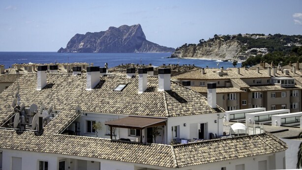 A coastal residential area with terracotta-tiled rooftops, a prominent rocky hill in the background, and a clear view of the sea. - Apartment Sunset Moraira City (Moraira)