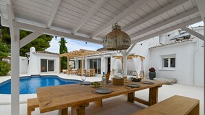 Ein überdachter Außenbereich mit Essbereich, einem Pool, Holzmöbeln und einem rustikalen Laternen.