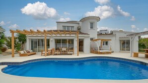 Ein modernes Haus mit Swimmingpool, Holzpergolen und Sitzgelegenheiten im Freien.
