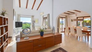 A spacious living area with a wooden ceiling, a sofa, a TV, and a dining area with chairs and a table. - Villa Vinalopo La Sella (Pedreguer)