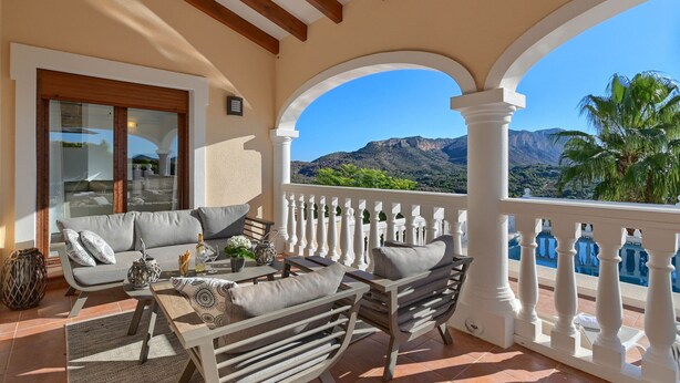 A balcony with a sofa, chairs, and a table, overlooking a mountainous landscape and a pool. - Villa Vinalopo La Sella (Pedreguer)