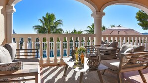 A balcony with a pool view, furnished with a sofa, chairs, and a table with drinks and snacks. - Villa Vinalopo La Sella (Pedreguer)