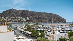 A marina with numerous boats docked, a road leading to the marina, and a hill with buildings in the background. - Apartment Octopus Moraira (Moraira)