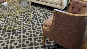 Una sala de estar moderna con un sofá beige, dos sillones, un tapete estampado y un ventilador de techo.