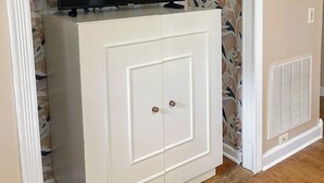 Un mueble blanco con un televisor de pantalla plana encima, un papel tapiz estampado y una rejilla en la pared.
