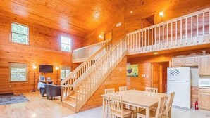L’intérieur d’une cabane en bois comprend un coin repas, une cuisine et un escalier menant à un niveau supérieur.