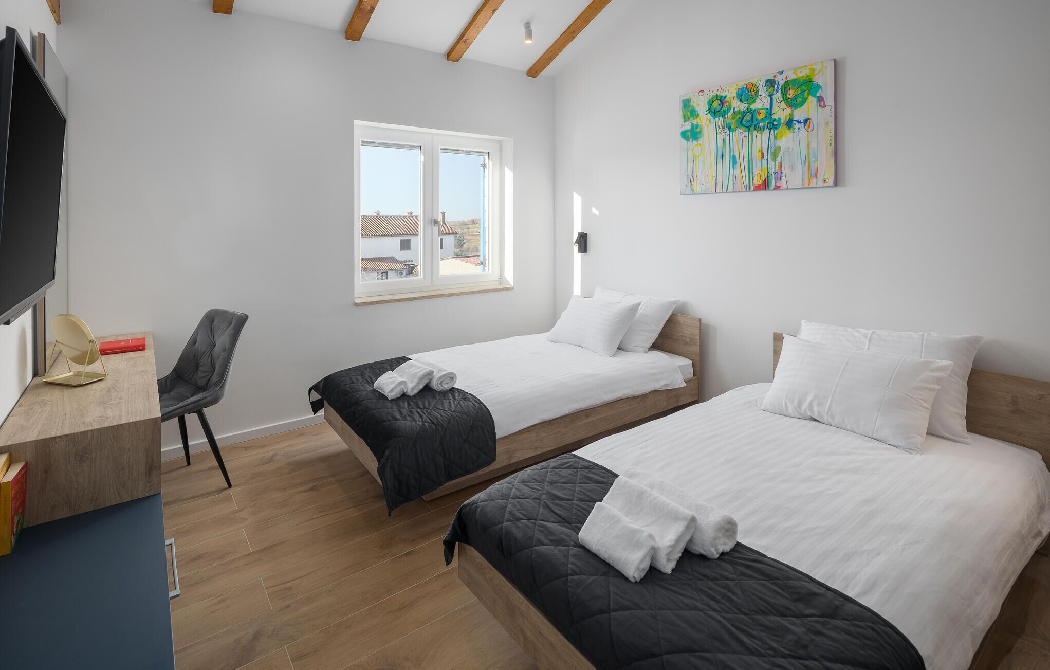 Ein modernes Hotelzimmer mit zwei Einzelbetten, einem Schreibtisch mit Stuhl, einem großen Fenster und einem Gemälde an der Wand.