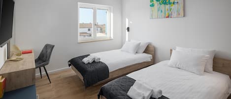 Ein modernes Hotelzimmer mit zwei Einzelbetten, einem Schreibtisch mit Stuhl, einem großen Fenster und einem Gemälde an der Wand.